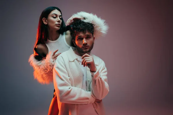 Young woman in faux fur jacket gesturing near pensive man posing on grey — Fotografia de Stock