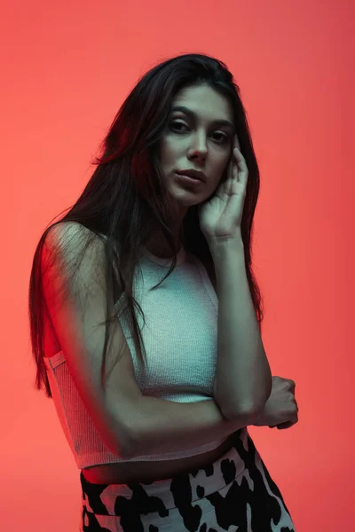 Brunette and young woman in tank top posing while looking at camera on red — Photo de stock