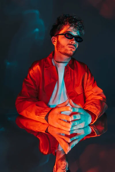 Stylish and curly young man in sunglasses posing with clenched hands on blue — Photo de stock