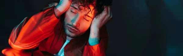 Curly and stylish man with closed eyes posing in orange shirt on blue, banner — Photo de stock