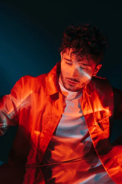 Lighting on face of curly and stylish man in orange shirt posing on blue - foto de stock