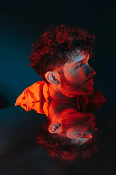 Reflection in mirror of curly and stylish man in orange shirt posing on blue — Stock Photo