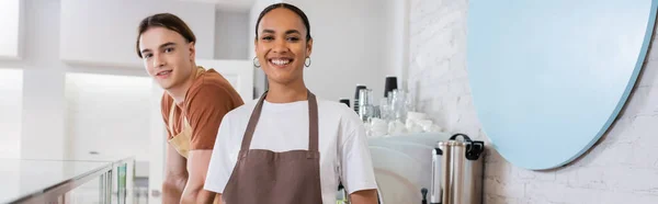 Smiling african american saleswoman looking at camera near colleague in confectionery, banner - foto de stock