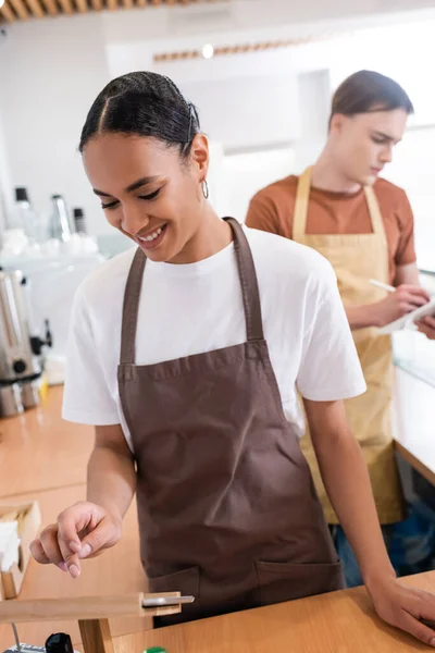 Smiling african american saleswoman in apron using digital tablet in sweet shop — Stock Photo