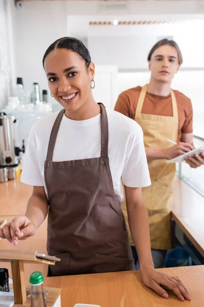 Cheerful african american saleswoman using digital tablet and looking at camera near colleague in confectionery — Stock Photo