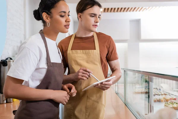 Young multiethnic sellers with digital tablet looking at showcase in confectionery — Fotografia de Stock