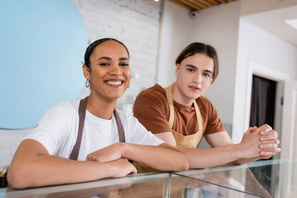 African american seller smiling at camera near colleague in confectionery — Stock Photo