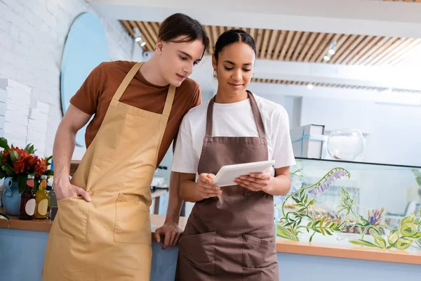 Multiethnic sellers in aprons using digital tablet in confectionery - foto de stock