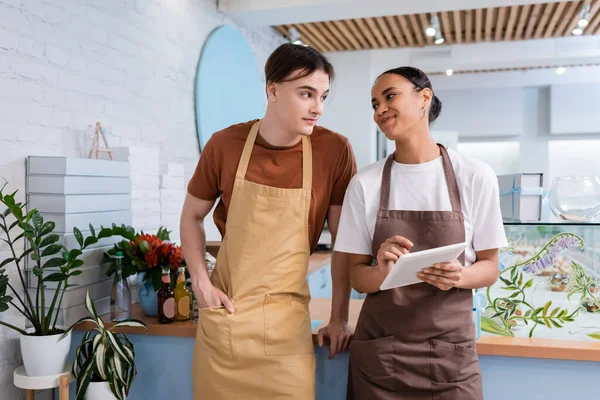 Smiling african american seller holding digital tablet and looking at colleague in sweet shop — Foto stock