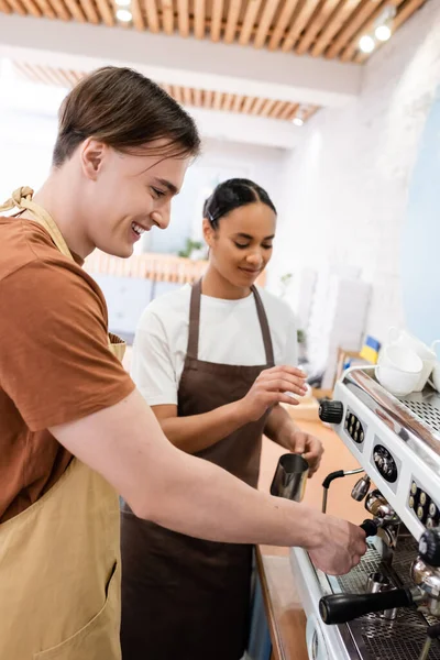 Smiling barista making coffee in machine near african american seller in confectionery - foto de stock