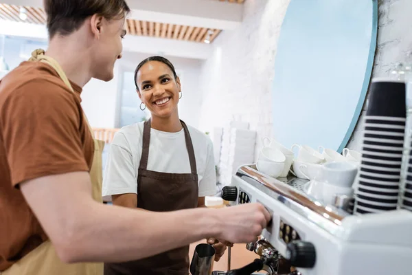 Lächelnder afrikanisch-amerikanischer Verkäufer mit Blick auf Barista, der Kaffee in Süßwaren kocht — Stockfoto