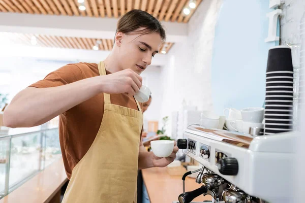 Young barista making coffee near machine in confectionery — стоковое фото