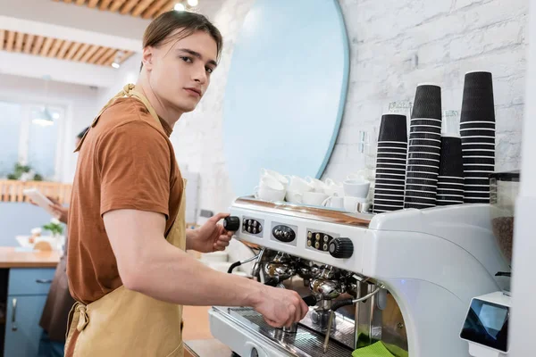 Barista in apron looking at camera while making coffee in sweet shop — Stock Photo
