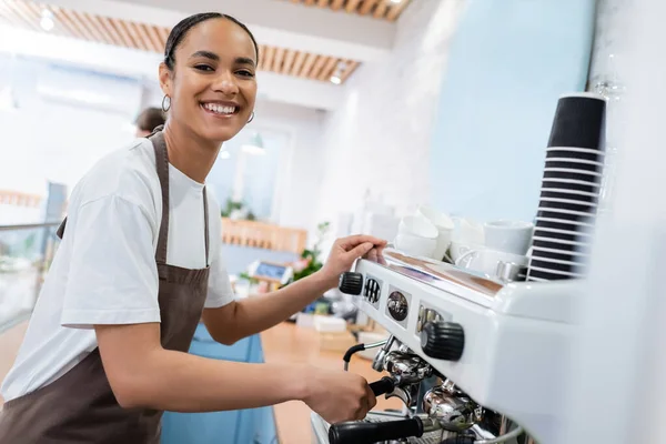 Fröhlicher afrikanisch-amerikanischer Barista, der Kaffee kocht und in Süßwaren in die Kamera schaut — Stockfoto