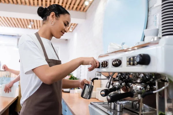 Seitenansicht eines jungen afrikanisch-amerikanischen Baristas, der in einem Süßwarenladen Kaffee auf einer Maschine kocht — Stockfoto