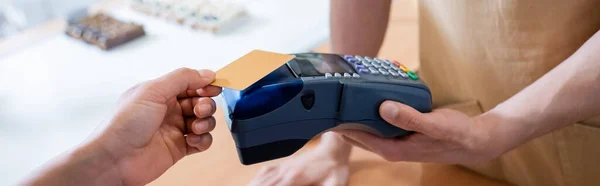 Cropped view of salesman holding terminal near african american customer with credit card in confectionery, banner — Photo de stock