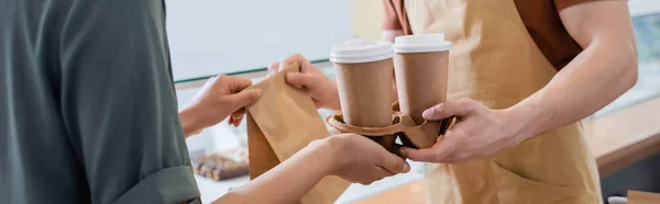 Cropped view of african american client taking coffee to go and paper bag from seller in sweet shop, banner — Photo de stock