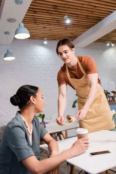 Smiling salesman giving dessert to african american client in confectionery — Stock Photo