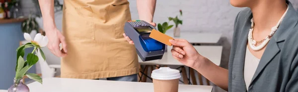 Cropped view of african american client paying with credit card near seller and coffee to go in sweet shop, banner - foto de stock