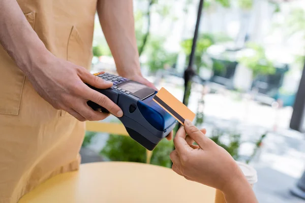Ausgeschnittene Ansicht eines afrikanisch-amerikanischen Kunden, der mit Kreditkarte in der Nähe von Verkäufer und Pappbecher auf der Süßwarenterrasse bezahlt — Stockfoto