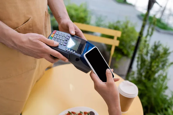 Cropped view of african american customer paying with smartphone near seller and blurred dessert on terrace of confectionery — Fotografia de Stock