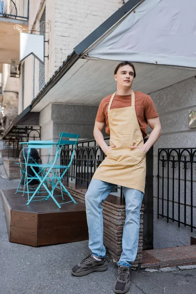 Smiling salesman in apron standing on terrace of confectionery outdoors — стоковое фото