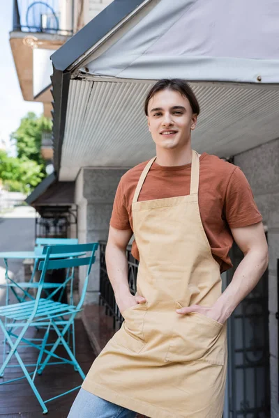 Positive salesman in apron looking at camera on terrace of sweet shop — Photo de stock