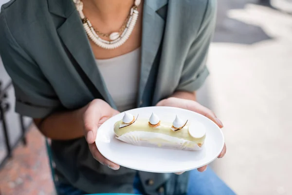 Cropped view of african american customer holding tasty eclair on terrace of confectionery — Foto stock