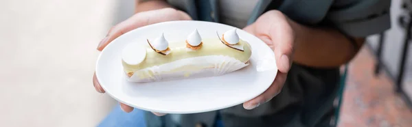 Cropped view of african american customer holding delicious dessert on terrace of sweet shop, banner — Photo de stock