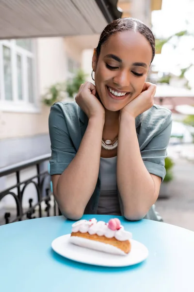 Позитивний афроамериканський клієнт дивиться на Еклера на терасі солодкого магазину — стокове фото