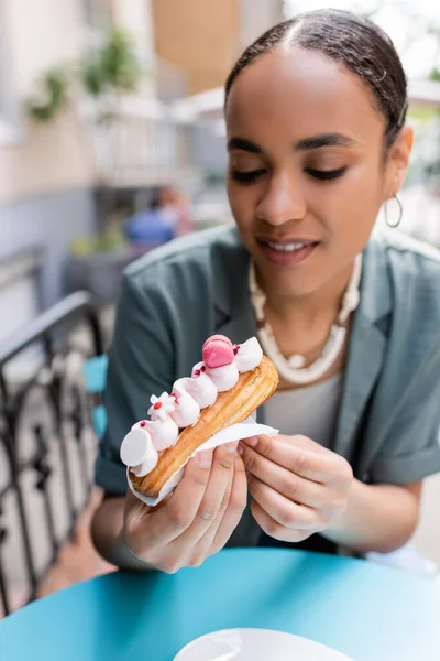 African american woman holding tasty dessert on terrace of sweet shop — стокове фото