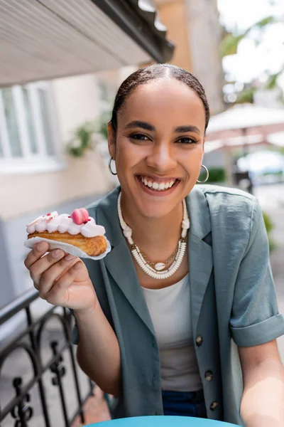 Young african american woman holding dessert and looking at camera on terrace of sweet shop — Fotografia de Stock