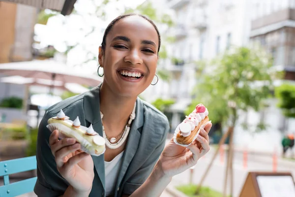 Positive african american customer holding eclairs on terrace of sweet shop — Fotografia de Stock