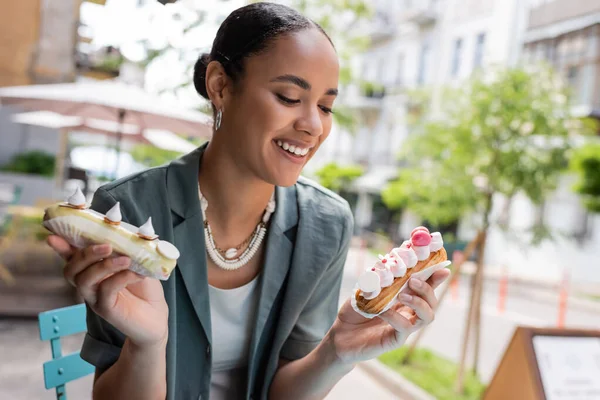 Young african american customer holding tasty eclairs on terrace of sweet shop - foto de stock