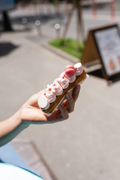 Cropped view of african american woman holding eclair with cream on terrace of confectionery — Fotografia de Stock