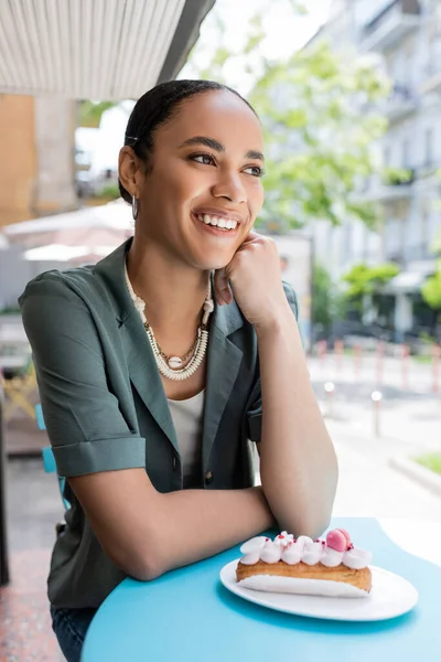 Smiling african american client sitting near tasty eclair on terrace of confectionery — Photo de stock