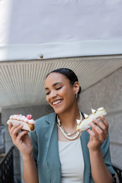 Hübsche afrikanisch-amerikanische Frau hält Eclairs auf der Terrasse eines Cafés — Stockfoto