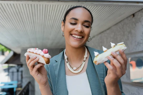Happy african american woman holding delicious eclairs near confectionery outdoors — стоковое фото