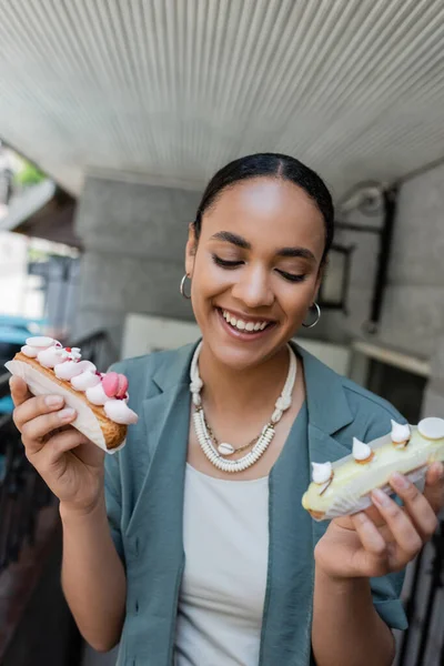 Positiver afrikanisch-amerikanischer Kunde hält Eclairs in der Nähe von Süßwaren im Freien — Stockfoto