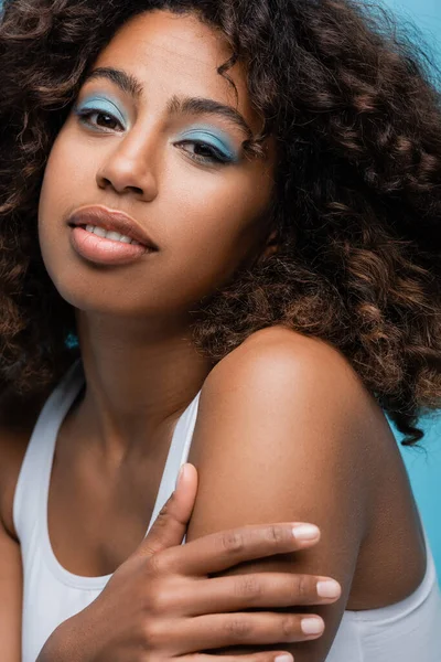 Portrait of african american woman with wavy hair and makeup on perfect face isolated on blue — стоковое фото