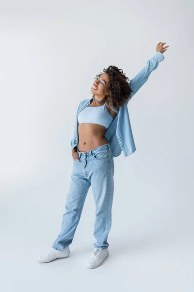 Full length of stylish african american woman with raised hand standing on grey background — стоковое фото
