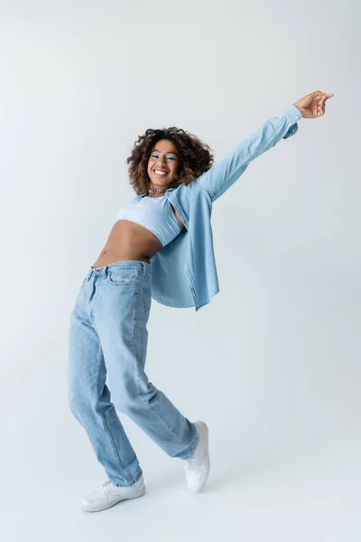 Full length of excited african american woman in crop top and blue denim clothes on grey background — Stockfoto
