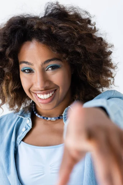 Happy african american woman with wavy hair looking at camera and pointing with finger isolated on grey — стоковое фото