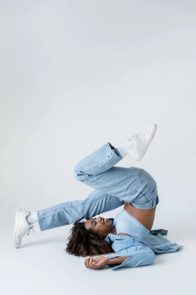 Side view of trendy african american woman in shoulder stand pose on grey background — Foto stock