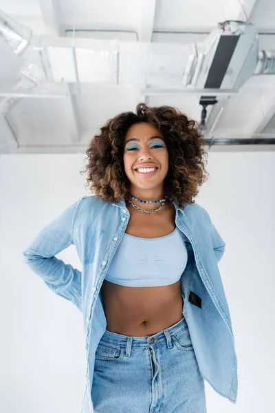 Happy african american woman in blue denim shirt and white crop top on white background — Photo de stock