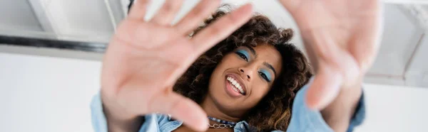 Bottom view of cheerful african american woman with blurred outstretched hands on grey background, banner — Stock Photo