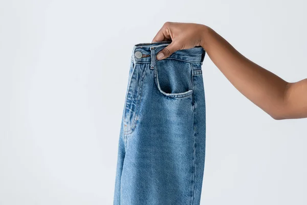 Partial view of african american woman holding blue cotton jeans isolated on grey - foto de stock