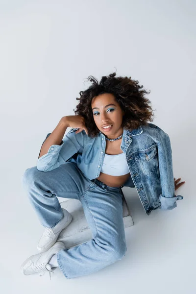 High angle view of african american woman in stylish denim clothing sitting on grey background — Foto stock