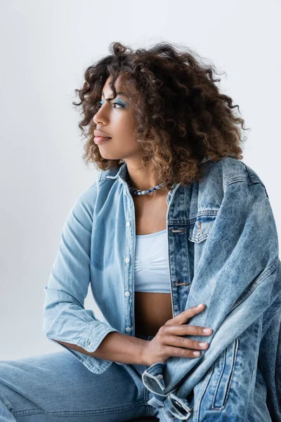 Trendy african american woman with wavy hair looking away isolated on grey - foto de stock
