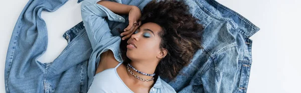 Top view of african american woman with closed eyes lying near denim clothing on grey background, banner — стоковое фото